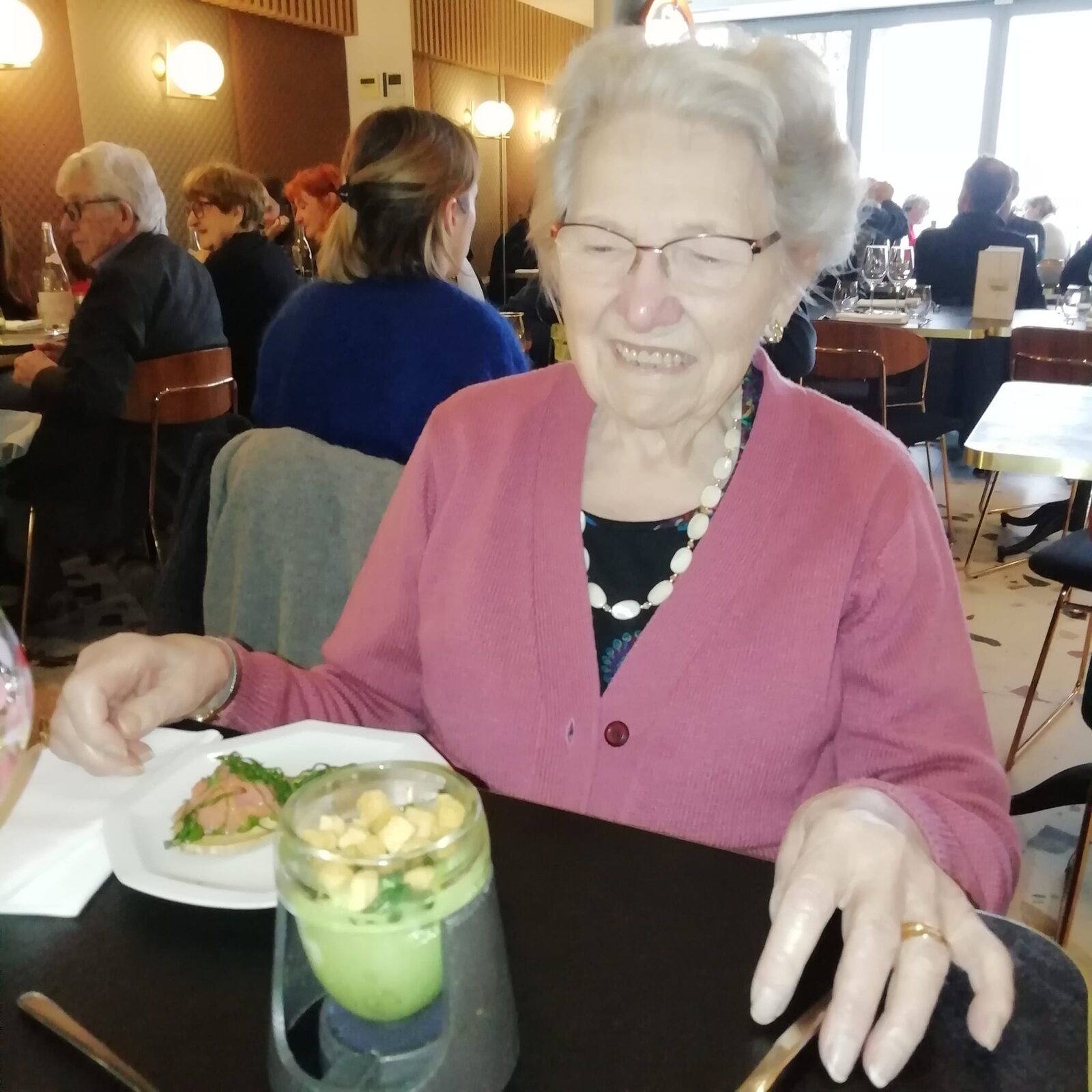 Yvonne en gilet rose, souriante, au restaurant